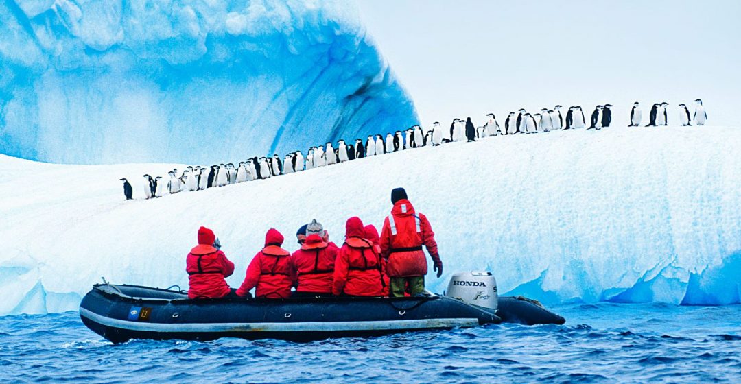 Tourists in a zodiac observe a colony of penguins on an ice ridge in Antarctica