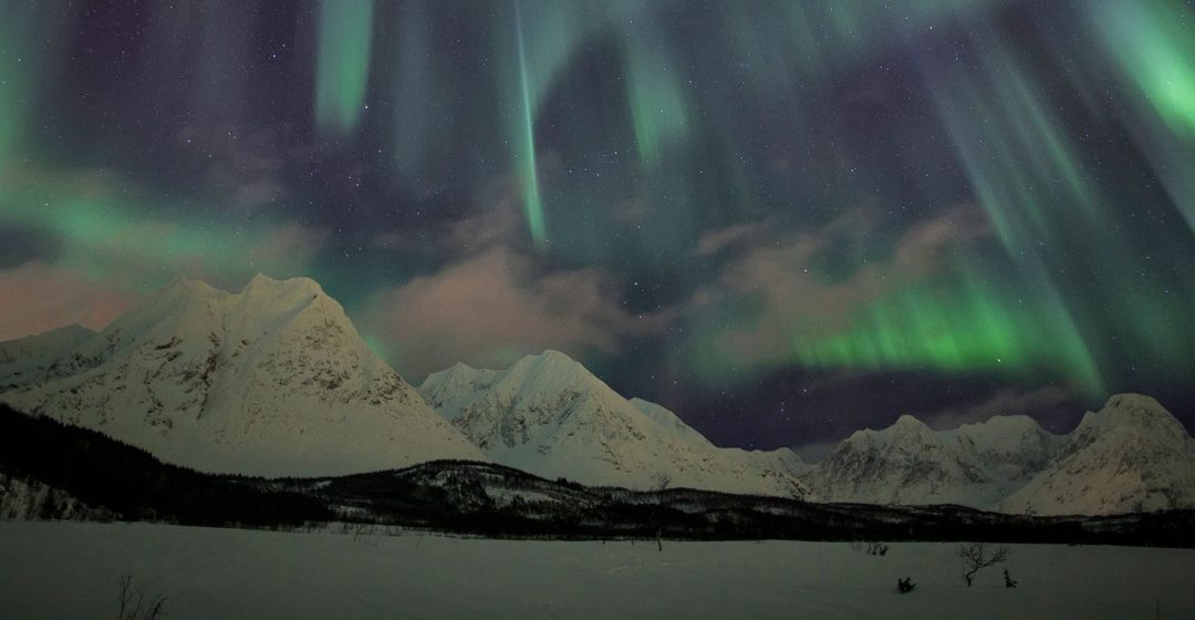 The Northern Lights illuminate the snowy landscape in Svensby Lyngen Alps, Tromsa, Norway