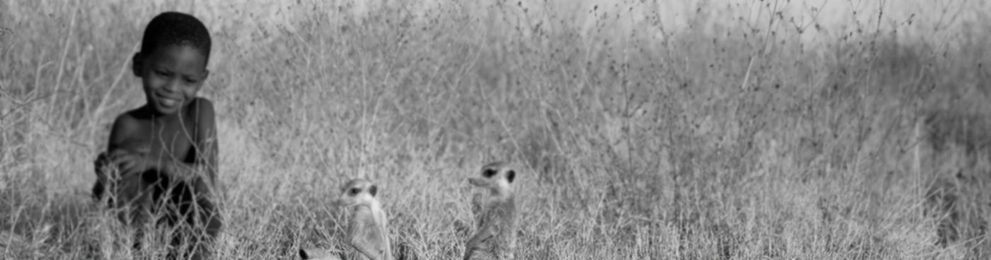 Botswana, Makgadikgadi, a bushman child watches a family of meerkats by the entrance to their burrow.