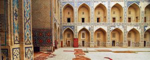 Uzbekistan, Bukhara, arched entrance in a row of historic buildings with carpets lying on courtyard.