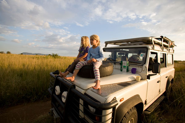 Young girls sit on the hood of their Land Rover as they look out over the game park, Masai Mara, Kenya