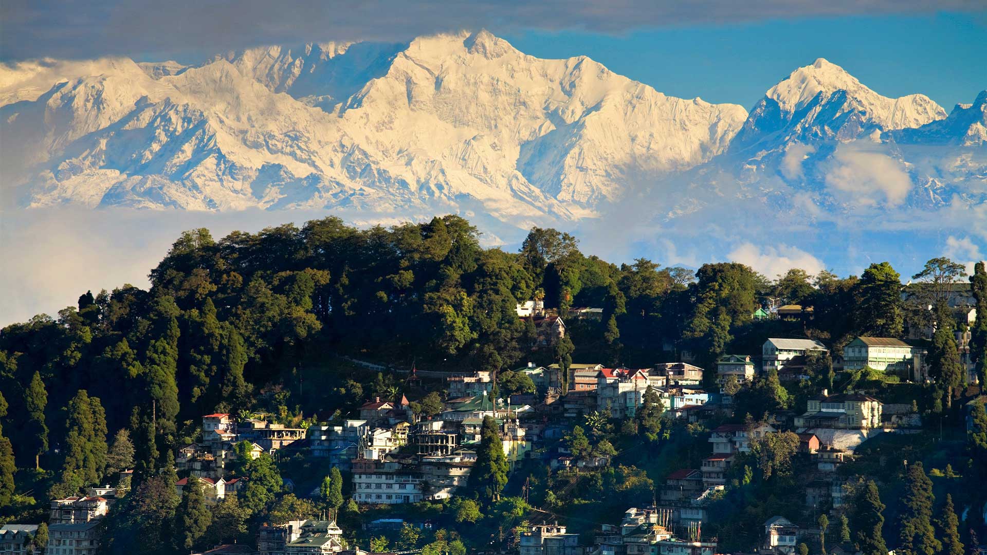 The town of Darjeeling perches on a hillside, with Mount Kanchenjunga behind in India with GeoEx.