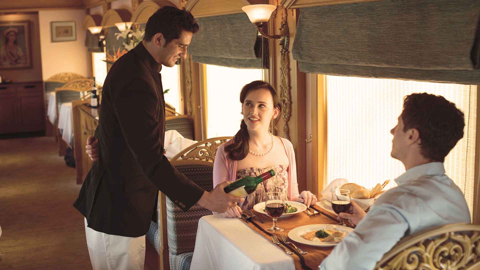 A couple is served wine with their elegant meal aboard the Deccan Odyssey train en route across India with GeoEx