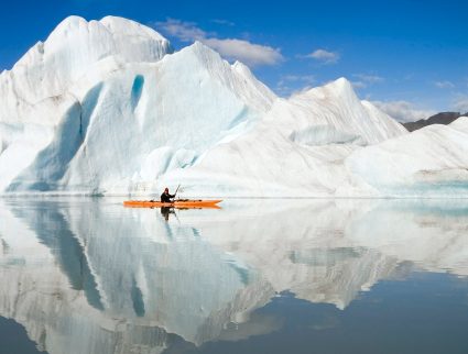 A kayaker paddles past an iceberg in the fjords of Alaska