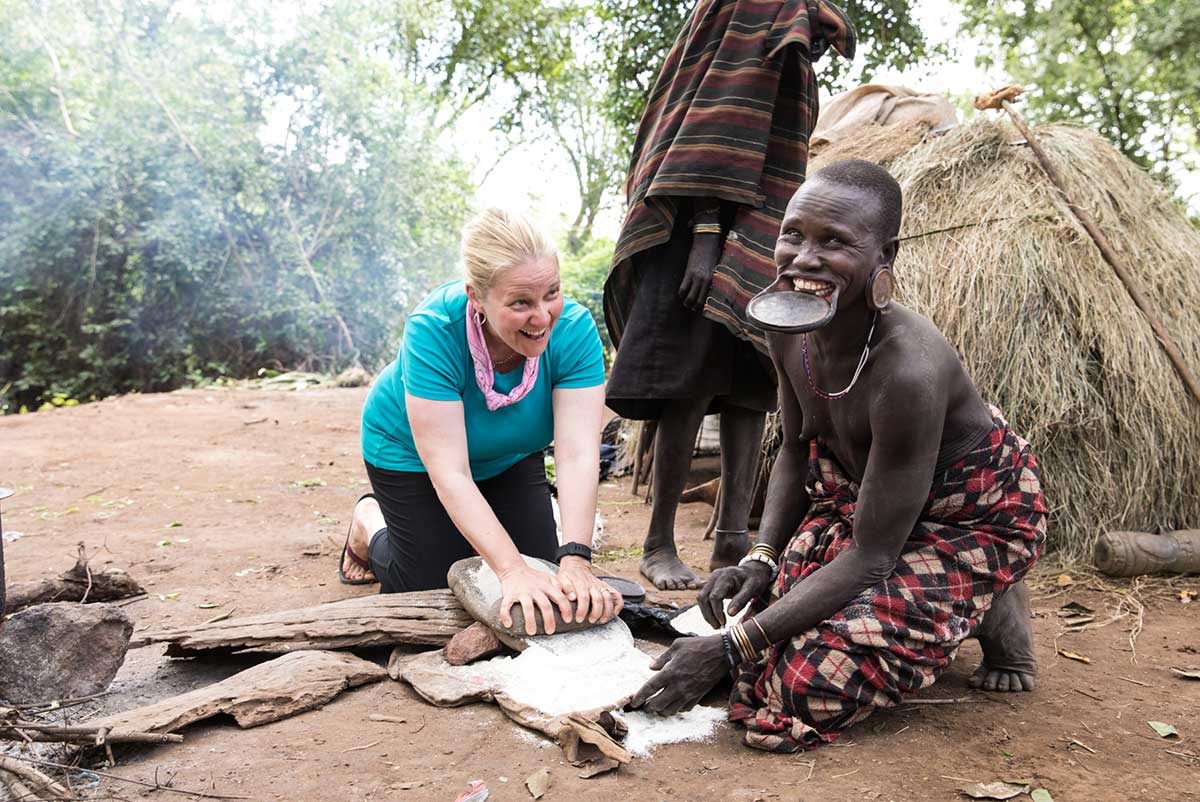 GeoEx traveler grinding flour during visit to the Mursi tribe