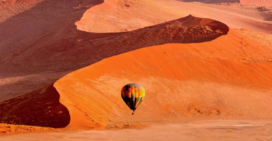 A hot air balloon floats across dunes in Namibia