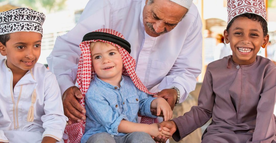 An Omani man helps a young European child shake hands with Omani children, Nizwa, Oman