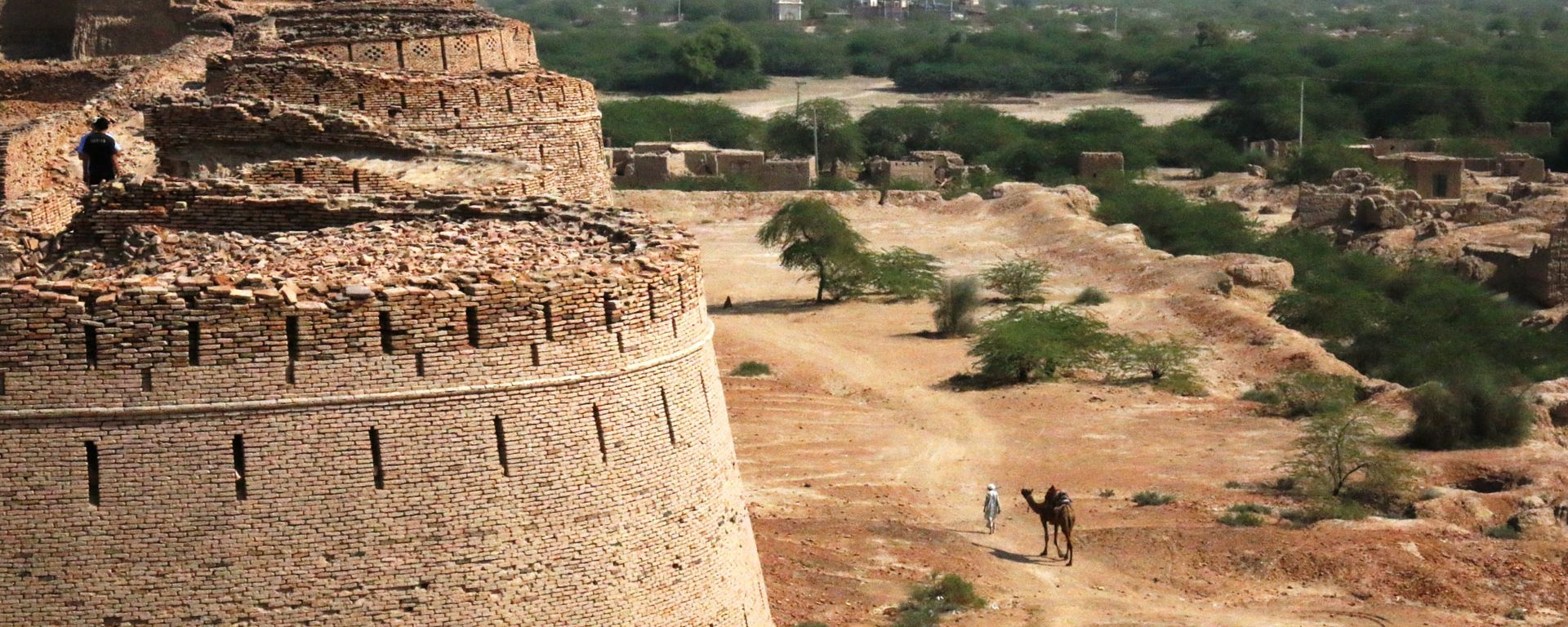 Man with camel walks outside Derawar Fort in Bahawalpur, Pakistan