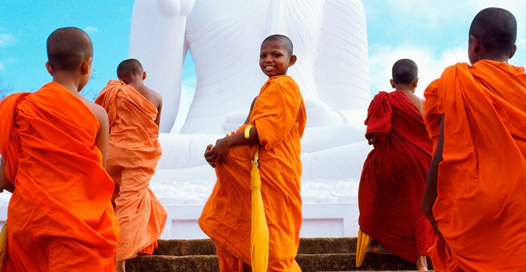 Group of young monks walking up steps in front of Buddha statue in Mihintale, Sri Lanka