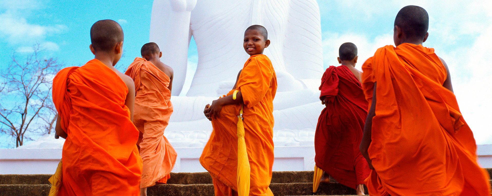 Group of young monks walking up steps in front of Buddha statue in Mihintale, Sri Lanka