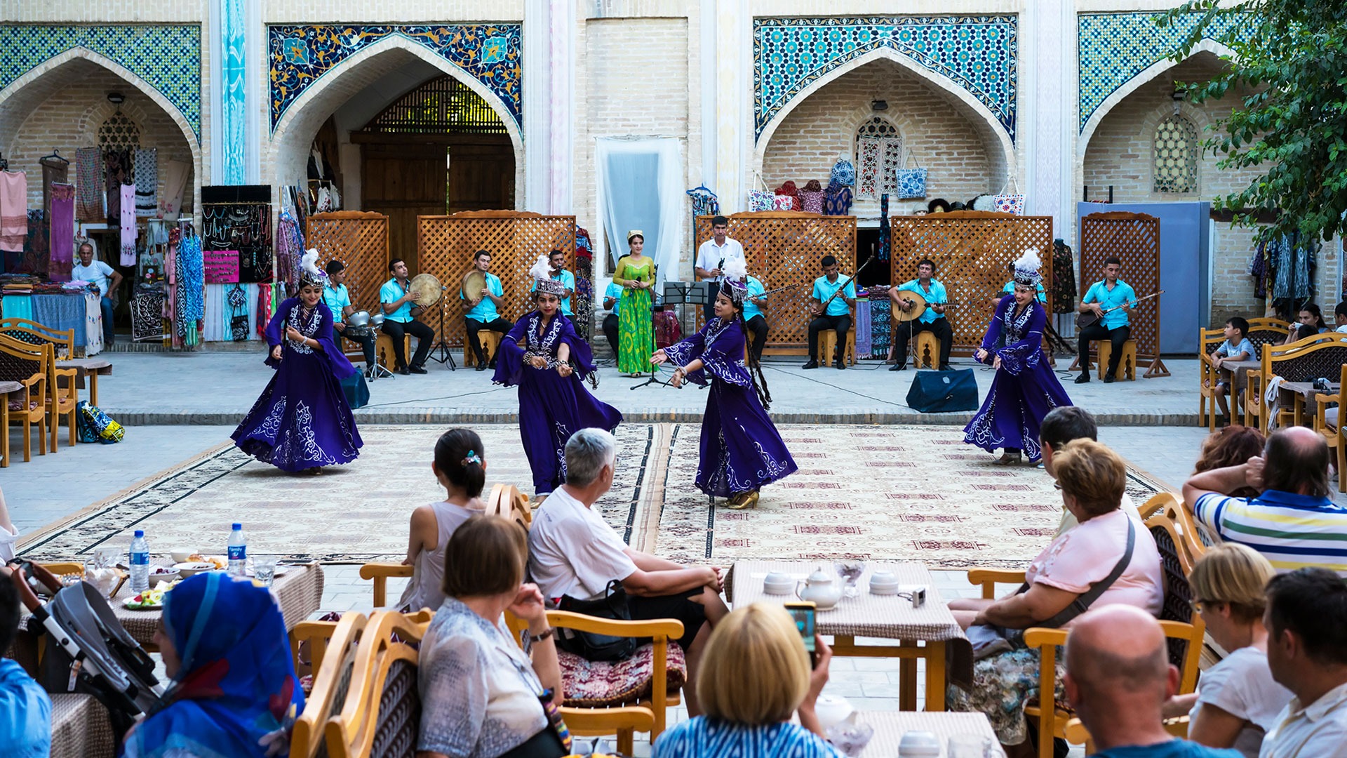 Tourists watching traditional Uzbek dance with souvenir shops in background in Bukhara, Uzbekistan